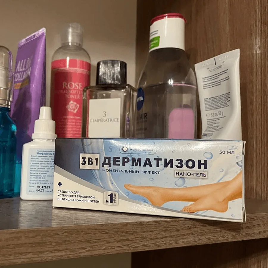 Упаковка геля Дерматизон лежит на полке рядом с другими флаконами, тюбиками, бутылочками