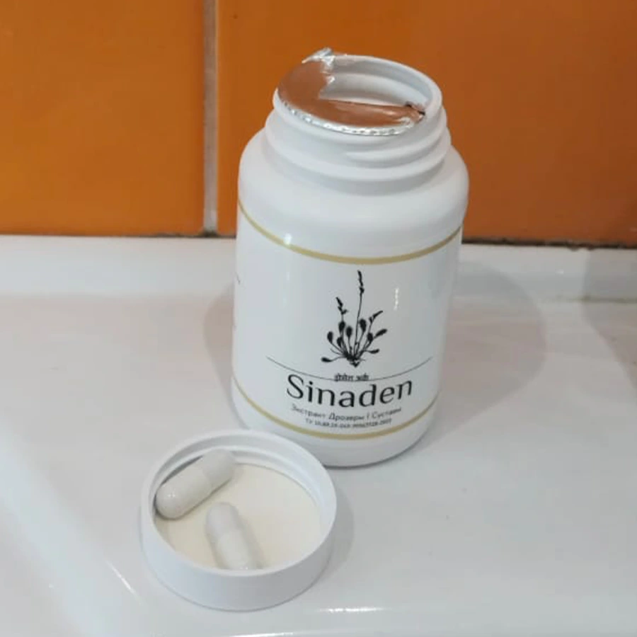 Открытая баночка с капсулами Синаден стоит на столе, две капсулы лежат в крышке