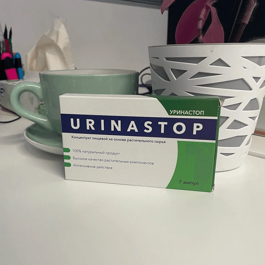 Упаковка Уринастоп стоит на столе на фоне зелёной кружке