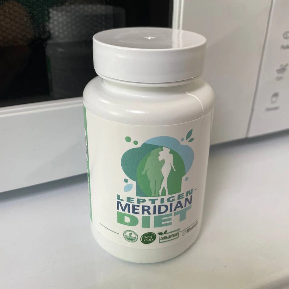 Пластиковая белая баночка с 60 капсулами Leptigen Meridian Diet стоит на фоне микроволновки