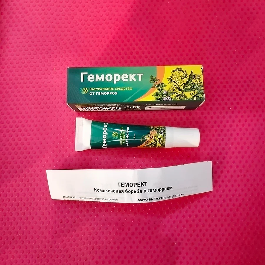 Картонная упаковка, тюбик с мазью Геморект и инструкция лежат на розовой ткани