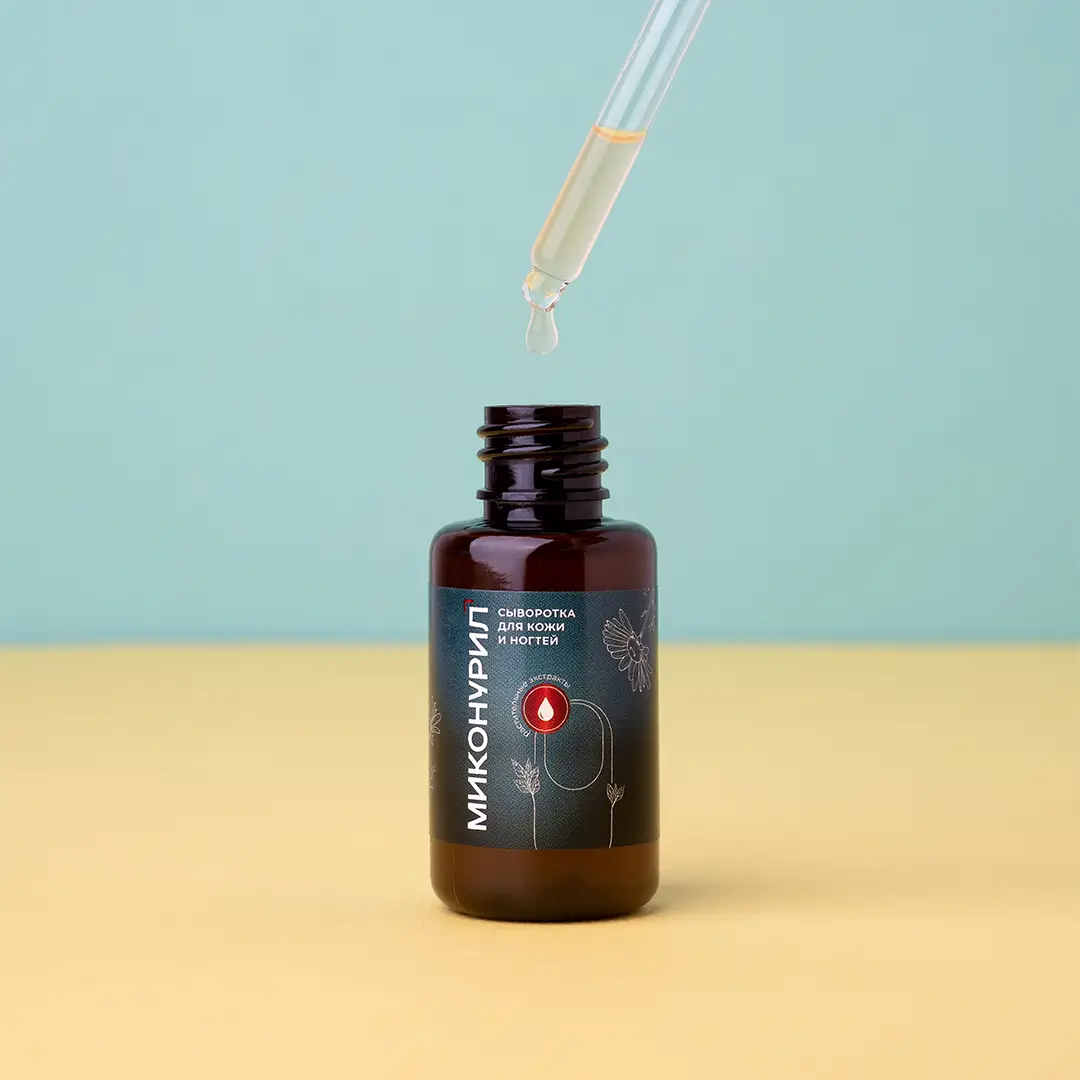 Флакон Миконурил с падающей каплей сыворотки из пипетки над горлышком. Флакон темно-коричневого цвета с зеленой этикеткой расположен на желтой поверхности на фоне мятно-зеленой стены