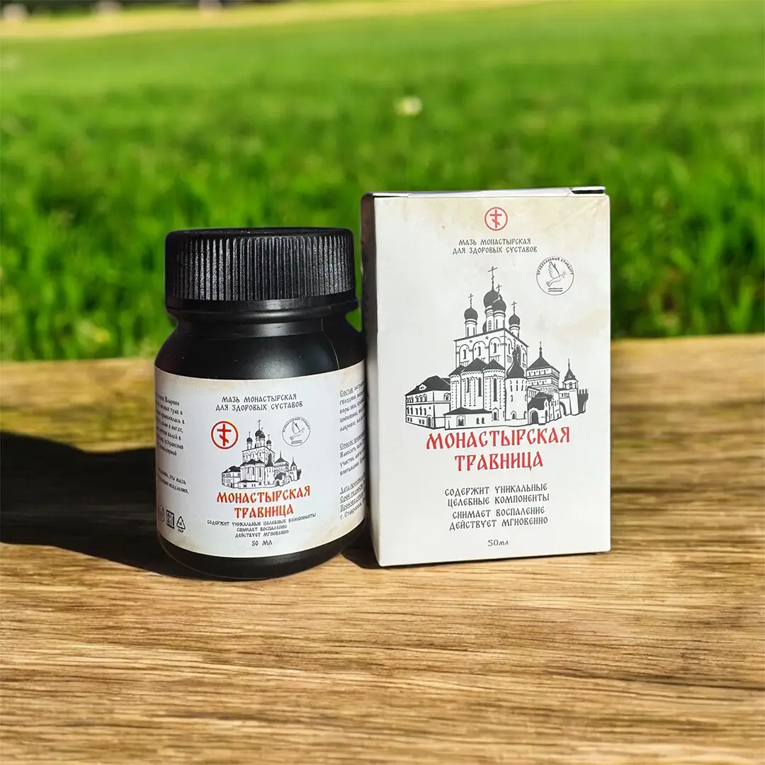 Темная банка с мазью Монастырская травница рядом с упаковкой на деревянной поверхности на фоне зеленой травы