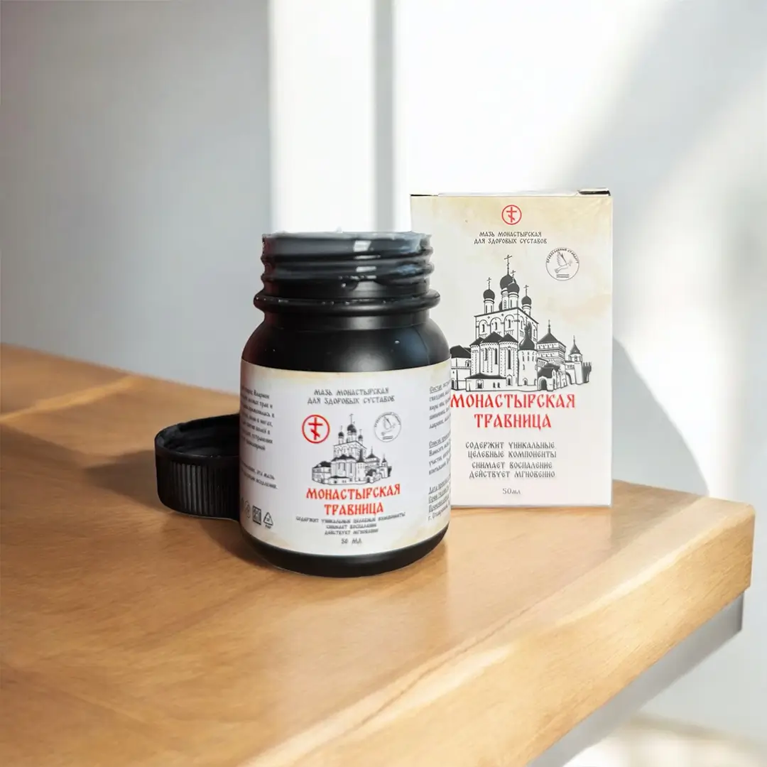 Открытая банка мази Монастырская травница без крышки рядом с упаковкой на деревянной полке у окна