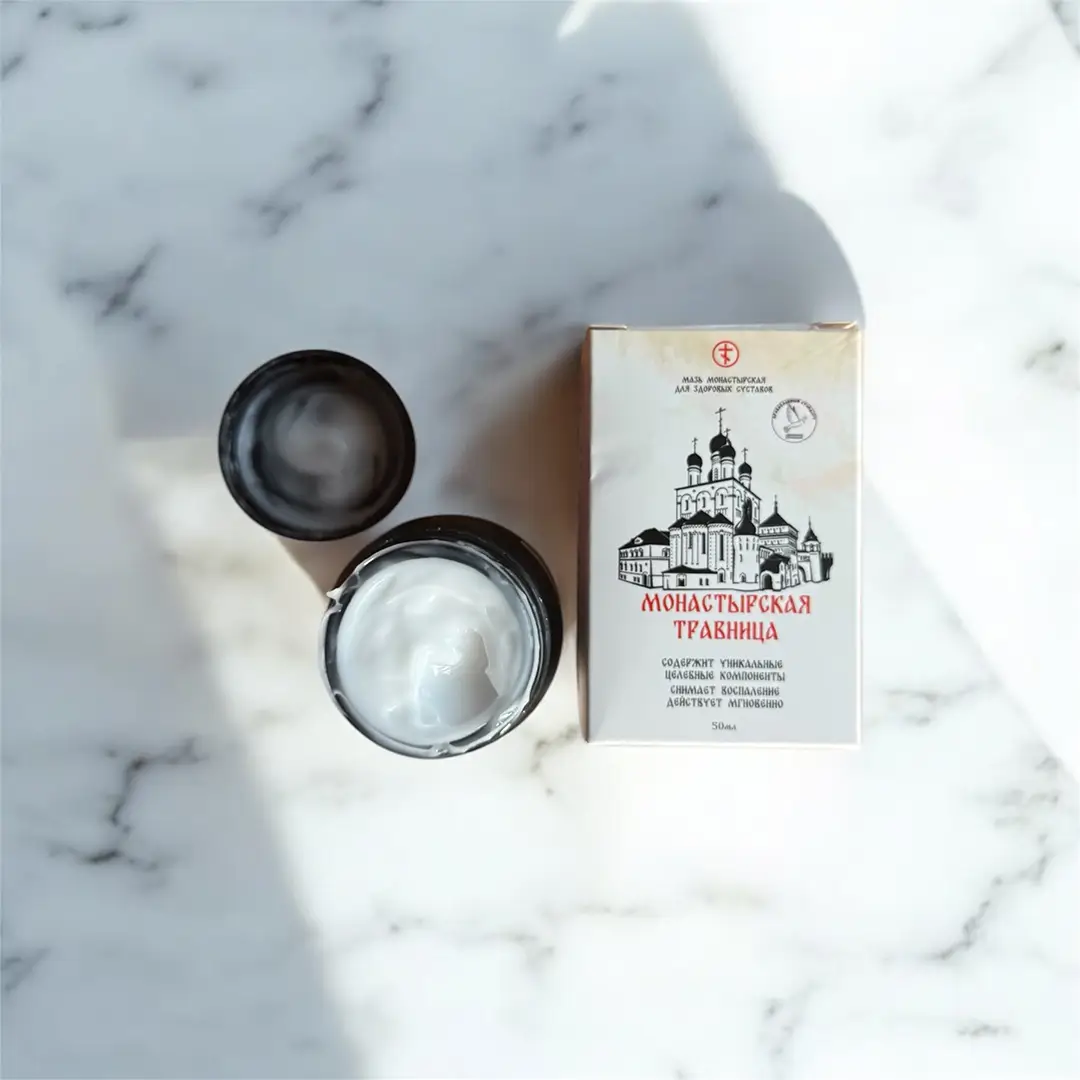 Вид сверху на мазь белого цвета в чёрной баночке, стоящей на мраморной поверхности